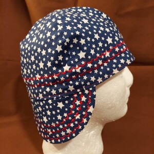 May include: A blue and white star-patterned hat with a red scalloped trim. The hat is designed with a brim and ear flaps. The hat is displayed on a white mannequin head.