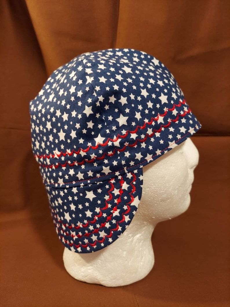 May include: A blue and white star-patterned hat with a red scalloped trim. The hat is designed with a brim and ear flaps. The hat is displayed on a white mannequin head.