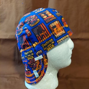 Peut inclure: Casquette de soudeur bleue avec un motif patchwork représentant des drapeaux américains, le texte "Pipefitter" et d'autres graphiques. La casquette a un bord incurvé et des rabats d'oreille, avec la taille 7 1/8 et 7 1/2 imprimée sur le côté.