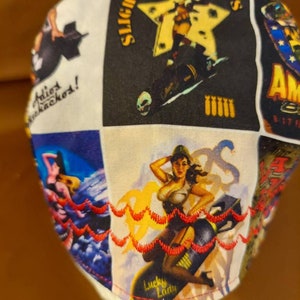 May include: White fabric cap with a patchwork design featuring vintage pin-up girl illustrations. The cap includes the text "Slightly Dangerous" and "Lucky Lady". The edges are trimmed with red decorative stitching.