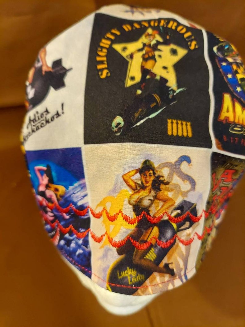May include: White fabric cap with a patchwork design featuring vintage pin-up girl illustrations. The cap includes the text "Slightly Dangerous" and "Lucky Lady". The edges are trimmed with red decorative stitching.