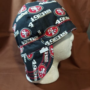 May include: Black welding cap featuring the San Francisco 49ers logo in red and gold. The cap has a repeating pattern of the team logo and the words "49ERS" in white. The cap is made in the USA.