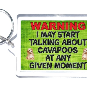 May include: A green and white key chain with a warning sign that reads "WARNING I MAY START TALKING ABOUT CAVAPOOS AT ANY GIVEN MOMENT". The key chain features two small, brown and white dogs.
