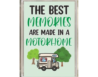 May include: A green and white rectangular sign with the text "THE BEST MEMORIES ARE MADE IN A MOTORHOME" in black text. A cartoon illustration of a beige motorhome with red curtains is in front of two green trees.