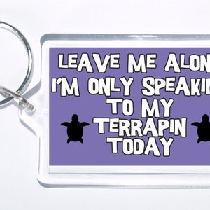 May include: Purple acrylic keychain with a white inscription that reads "Leave me alone I'm only speaking to my terrapin today". Two black turtle silhouettes are on either side of the text.