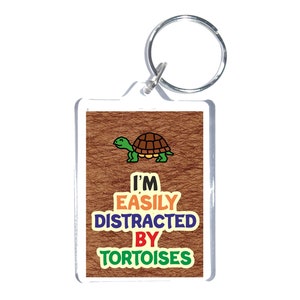 May include: A brown and white key chain with a cartoon tortoise and the text "I'm Easily Distracted By Tortoises".
