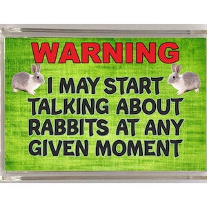 Peut inclure: Un panneau d'avertissement vert et blanc avec le texte "WARNING I MAY START TALKING ABOUT RABBITS AT ANY GIVEN MOMENT". Deux lapins blancs avec des taches noires sont de chaque côté du texte.