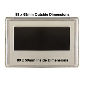 May include: A clear plastic frame with a black rectangular magnet inside. The frame has the text "99 x 68mm Outside Dimensions" and "89 x 59mm Inside Dimensions" printed on it.