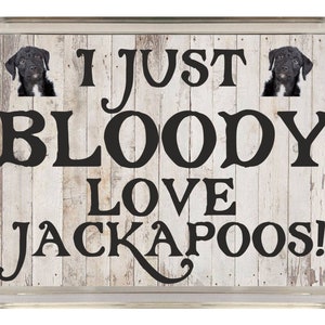 Puede incluir: Un letrero de madera blanca con texto negro que dice "Me encantan los Jackapoos!" Dos perros Jackapoo negros y blancos asoman por detrás del texto.