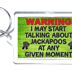 May include: A green and white warning sign keychain with a black and white dog image. The text on the sign reads "WARNING I MAY START TALKING ABOUT JACKAPOOS AT ANY GIVEN MOMENT".