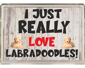 Könnte beinhalten: Ein weißes Holzschild mit dem Text "I just really love Labradoodles!" in schwarzen und roten Buchstaben. Zwei Labradoodle sind auf beiden Seiten des Textes abgebildet.
