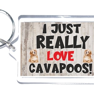 May include: A white key chain with a woodgrain background and two small dogs. The text on the key chain reads "I Just Really Love Cavapoos!" in black and red lettering.