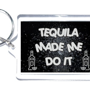May include: A rectangular keychain with a silver ring. The keychain has a white border and a black background with the text "TEQUILA MADE ME DO IT" in white. Two tequila bottle illustrations are on the keychain.