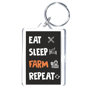 May include: A rectangular keychain with a black background and the words "EAT SLEEP FARM REPEAT" in white and orange. The keychain has a silver metal ring attached to the top.
