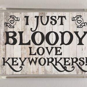 May include: A white wooden sign with black text that reads "I just bloody love keyworkers!" The sign has two black hand-drawn hearts with hands holding them on either side of the text.