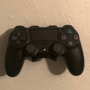 Puede incluir: Un mando de PlayStation 4 negro con un logotipo de PlayStation en blanco y negro en la parte delantera. El mando tiene un pad direccional, cuatro botones de cara, dos sticks analógicos y dos botones de hombro.