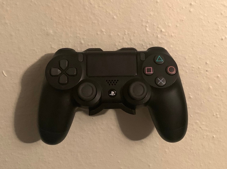 May include: A black PlayStation 4 controller with a black and white PlayStation logo on the front. The controller has a directional pad, four face buttons, two analog sticks, and two shoulder buttons.