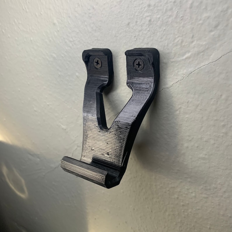 Puede incluir: Un soporte de pared de pl&aacute;stico negro con dos agujeros para tornillos. El soporte est&aacute; dise&ntilde;ado para sujetar un mando u otro dispositivo.