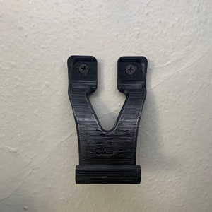 Puede incluir: Un soporte de pared de pl&aacute;stico negro con dos agujeros para tornillos. El soporte tiene forma de V y una base plana.