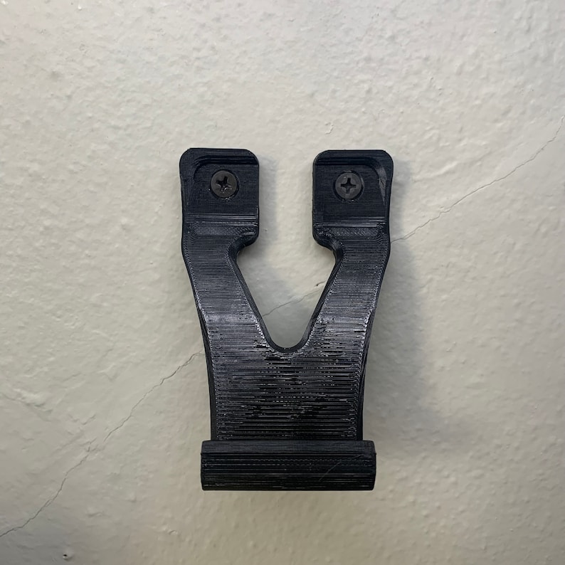 Puede incluir: Un soporte de pared de pl&aacute;stico negro con dos agujeros para tornillos. El soporte tiene forma de V y una base plana.