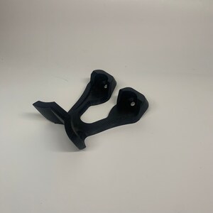 May include: Two black plastic wall mounts for hanging items. The mounts have a curved shape and a small hole in the center.