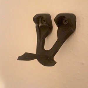 May include: A black plastic wall mount with two screw holes. The mount is shaped like a stylized letter Y.