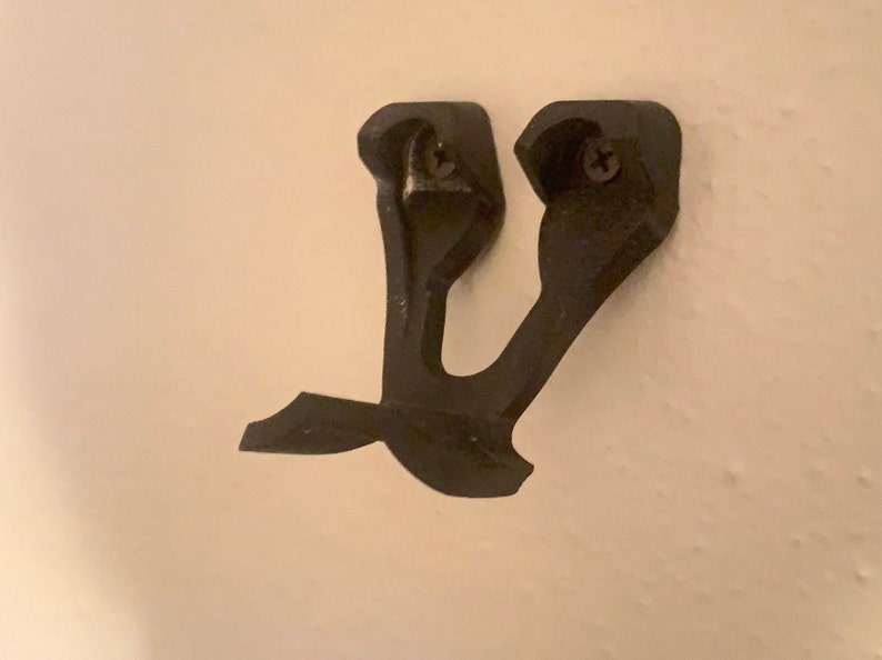 May include: A black plastic wall mount with two screw holes. The mount is shaped like a stylized letter Y.