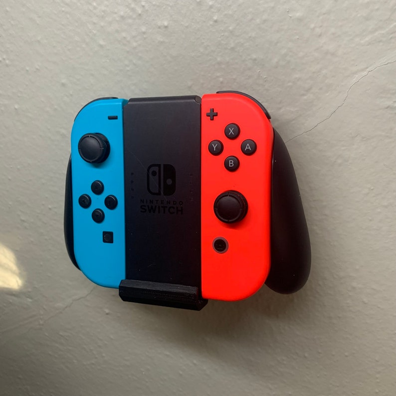 Puede incluir: Un mando de Nintendo Switch azul y rojo con botones negros y un panel central negro. El mando tiene el logotipo de Nintendo Switch y el texto "NINTENDO SWITCH" impreso en &eacute;l.