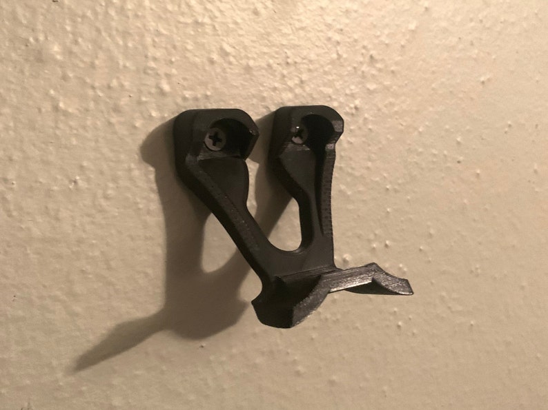 May include: A black plastic wall mount with two screw holes. The mount is designed to hold a gaming controller.