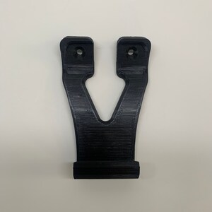 Puede incluir: Un soporte de pared de pl&aacute;stico negro con dos agujeros para tornillos. El soporte tiene forma de V y una base plana.