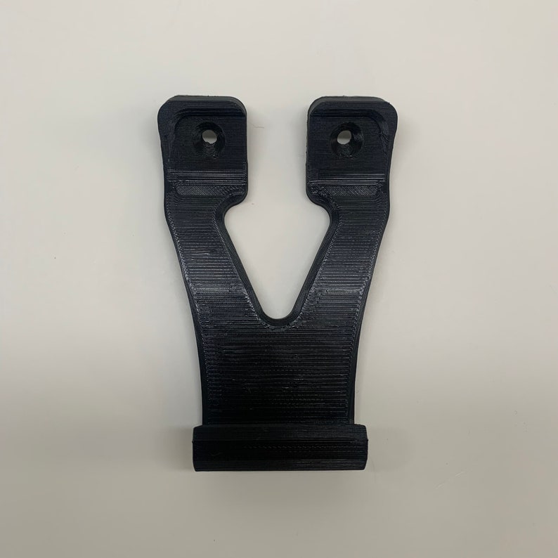 Puede incluir: Un soporte de pared de pl&aacute;stico negro con dos agujeros para tornillos. El soporte tiene forma de V y una base plana.