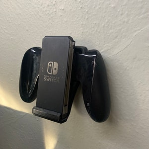Puede incluir: Un soporte de mando negro para Nintendo Switch con las palabras "Nintendo Switch" impresas en la parte delantera.