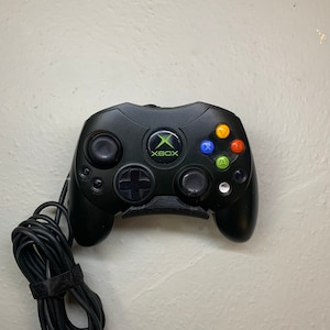 May include: A black Xbox controller with a green Xbox logo and colored buttons. The controller is connected to a black cord.