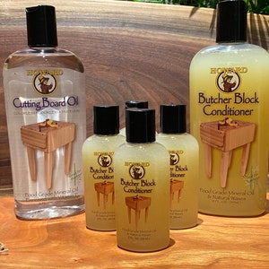 May include: Four bottles of Howard Butcher Block Conditioner and one bottle of Howard Cutting Board Oil. The bottles are clear and show the product inside. The bottles are on a wooden surface.