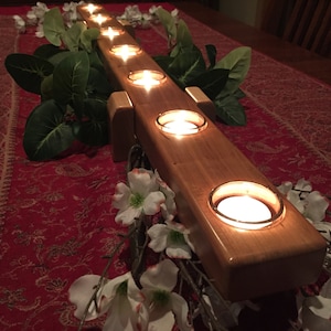 May include: A wooden candle holder with six candle slots. The holder is made of light brown wood and has a natural finish. The candles are lit and casting a warm glow.