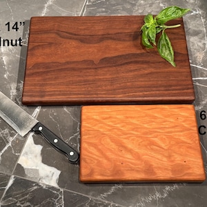 May include: A rectangular dark brown walnut cutting board measuring 9 inches by 14 inches and a smaller rectangular light orange cherry cutting board measuring 6 inches by 9 inches, accompanied by a stainless steel chef knife with a black handle.
