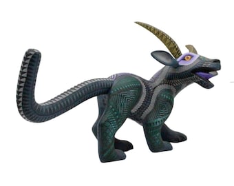 May include: A hand-carved wooden alebrije sculpture of a mythical creature with a long tail, curved horns, and an open mouth. The figure is painted in dark blue, green, and purple tones with intricate, geometric patterns covering its entire body.