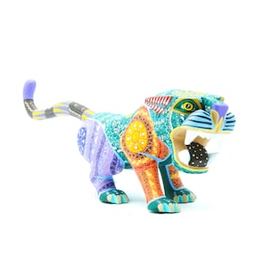 May include: A vibrantly painted wooden jaguar figurine. The sculpture features intricate patterns in teal, orange, purple, and yellow. The jaguar is posed with an open mouth, showcasing its teeth, and has a long tail.