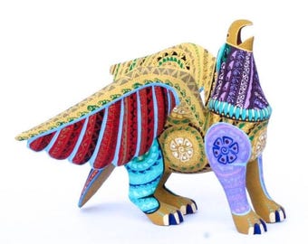 May include: A hand-painted wooden sculpture of a mythical creature with wings, featuring intricate patterns in shades of gold, red, blue, purple, and turquoise. The figure has a bird-like head with an open beak and four legs with claws.