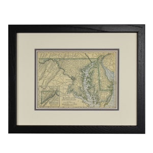 May include: Framed vintage map of Maryland and Delaware, featuring detailed cartography in shades of green, beige, and brown. The map is set within a cream-colored mat and a black wooden frame, suitable for home decor.