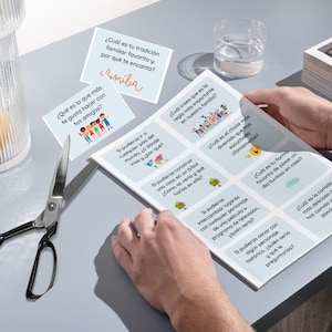 May include: A set of blue and white cards with Spanish text and illustrations. The cards feature questions about family, friends, and personal preferences. The cards are laid out on a gray surface.