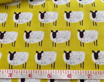 May include: Yellow fabric with a repeating pattern of white sheep with black faces and legs. A measuring tape is laid across the bottom, showing inches. The sheep are spaced evenly across the fabric.