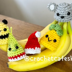Könnte beinhalten: Fünf gehäkelte Fingerpuppen auf einem Stapel Bananen. Die Puppen sind ein gelber Ananas, ein grüner und roter Weihnachtsbaum, eine gelbe und schwarze Biene, eine rote Weihnachtsmütze und eine graue Maus.