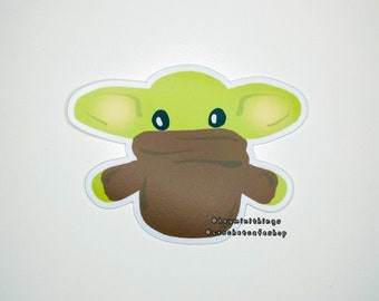May include: A green and brown cartoon sticker of a character wearing a brown scarf. The sticker has the text "@heymini.things @crochetcafe.shop" on the bottom.