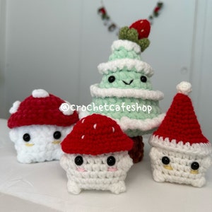 Pode incluir: Quatro enfeites de Natal de crochê: uma árvore de Natal verde com um morango vermelho e verde no topo, um cogumelo vermelho e branco, um cogumelo vermelho e branco e um boneco de neve branco com um chapéu de Papai Noel vermelho.