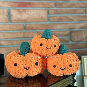 May include: Three crocheted orange pumpkins with green stems and black eyes and smiles. The pumpkins are stacked on top of each other. The image includes the text "@crochetcafeshop".
