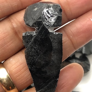 May include: A black obsidian arrowhead with a pointed tip and a flat base. The arrowhead has a smooth, polished surface and is approximately 2 inches long.