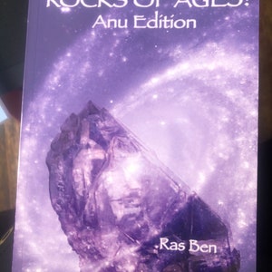 May include: A book cover with a purple background and a large, dark purple crystal. The title of the book is "Rocks of Ages: Anu Edition" and the author is "Ras Ben".