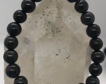 May include: A black beaded bracelet. The bracelet is made of smooth, round, black beads strung together. The beads have a glossy finish and are evenly sized. The bracelet is displayed against a light background.
