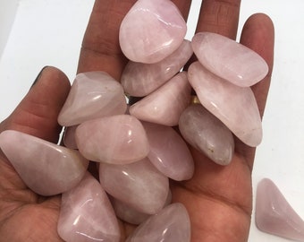 May include: A collection of tumbled rose quartz stones in various sizes and shapes. The stones are a pale pink color and have a smooth, polished finish.
